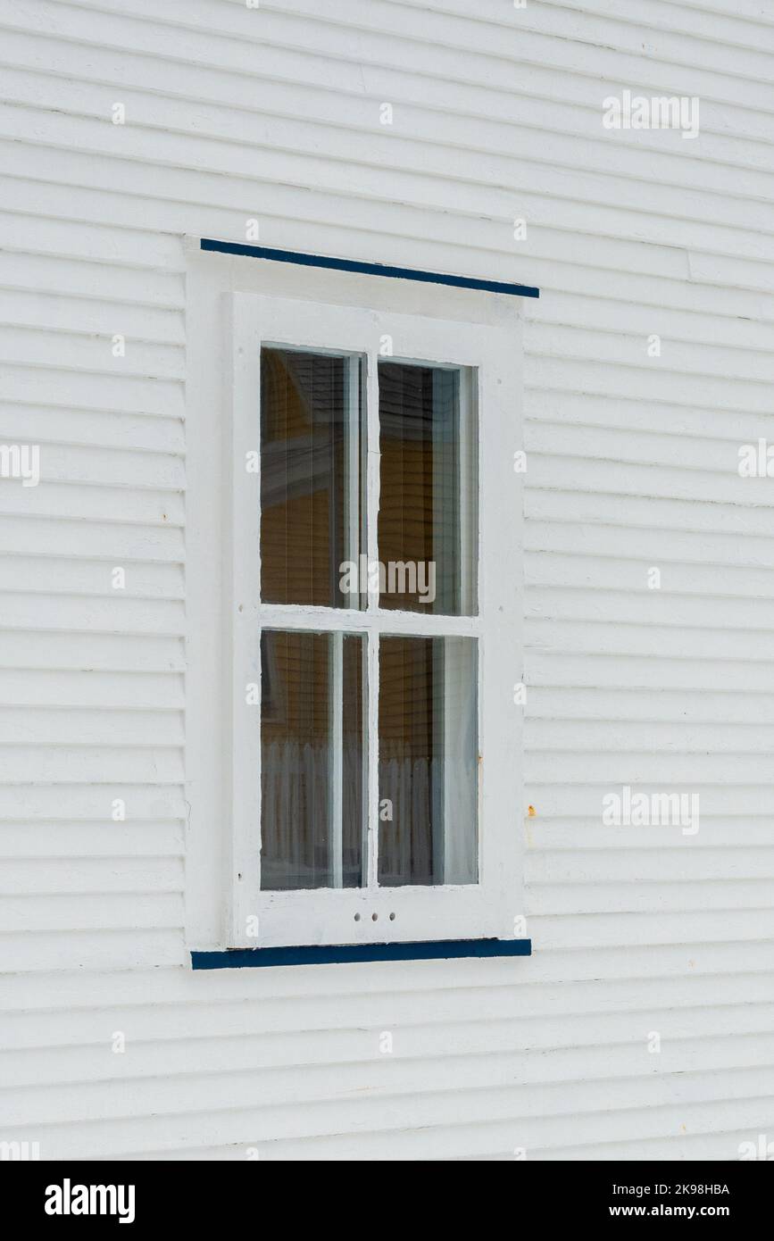 A small single casement window in a white narrow wood beveled clapboard siding exterior wall of a vintage house. The glass window has four panes. Stock Photo