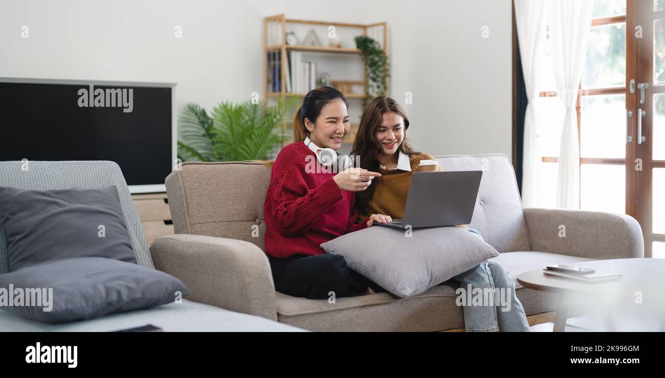 Asian woman friends sitting in living room watching movie on laptop together. Modern female friendship enjoy weekend activity lifestyle with wireless Stock Photo