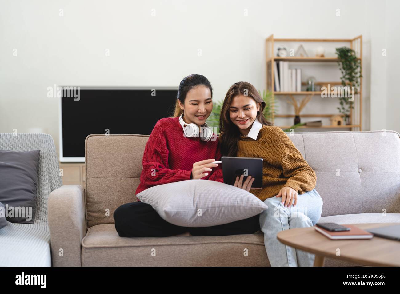 Asian woman friends sitting in living room watching movie on tablet together. Modern female friendship enjoy weekend activity lifestyle with wireless Stock Photo