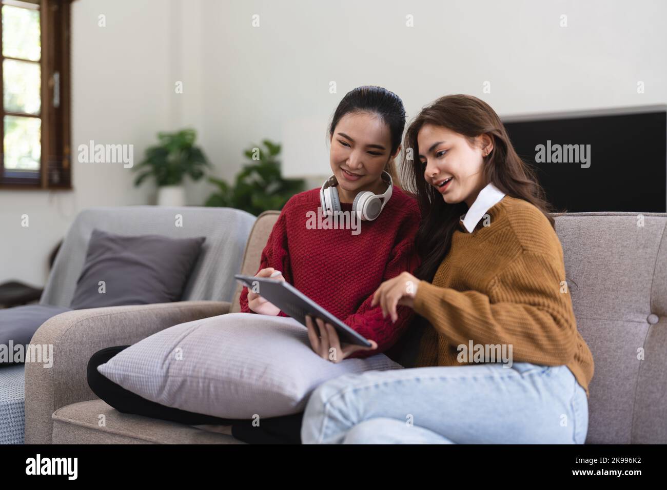 Asian woman friends sitting in living room watching movie on tablet together. Modern female friendship enjoy weekend activity lifestyle with wireless Stock Photo