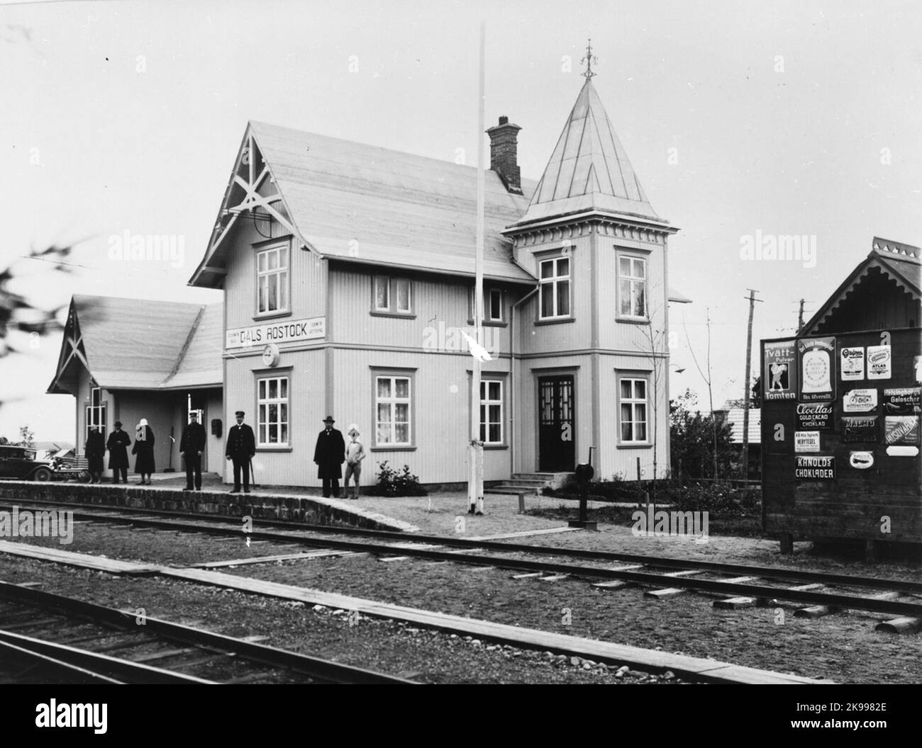 The railway station in Dals-Rostock. The side building on the left was used at the original stop in Rostock, built in 1884, and was originally located above Rostock's well. Later, the building was transported down to the place where the Dals-Rostock railway station was erected in 1908, and was then expanded to station houses. In 1941 the station house was demolished and replaced with a new one. Today, in Dals-Rostock, there is a model in scale 1: 2 of the original station house. Advertising: Lagerman's washing powder Santa; Malmö Stora Walsqvarn; Gripen Velocipeder; Atlas rubber rings; Puch mo Stock Photo