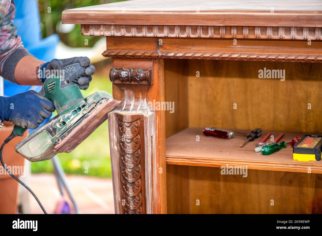 A Woman using a grinder removes old paint from furniture, restoration