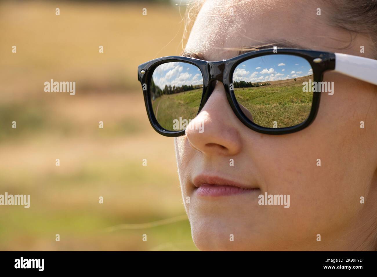 face of a girl in sunglasses closeup, reflections in glasses of the field and sky in summer Stock Photo