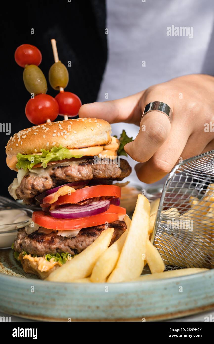 close up on burger in a plate and hands of unknown caucasian man prepare to eat on the table in sunny day outdoor at restaurant Stock Photo