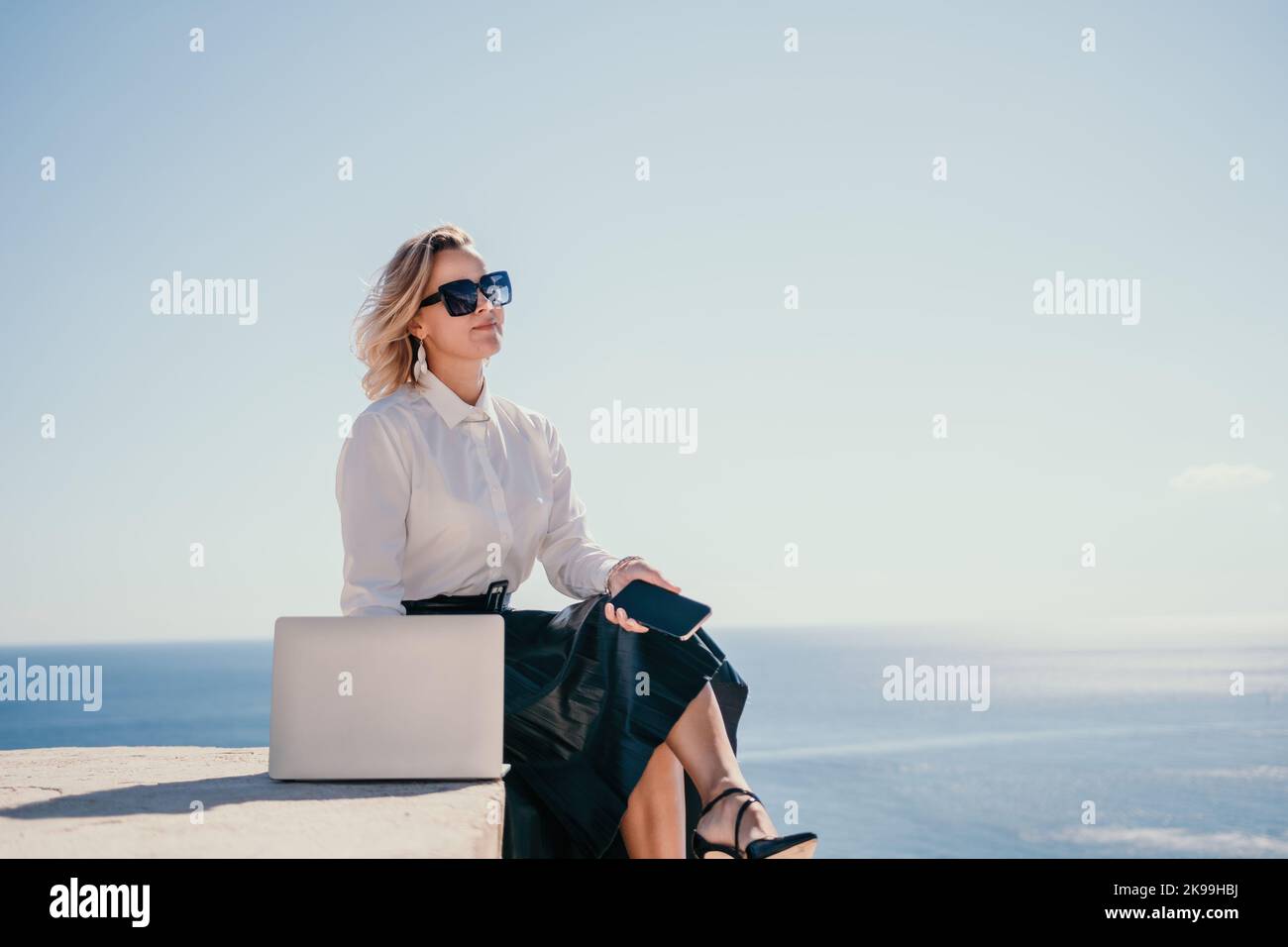 Digital nomad, Business woman working on laptop by the sea. Pretty lady typing on computer by the sea at sunset, makes a business transaction online Stock Photo