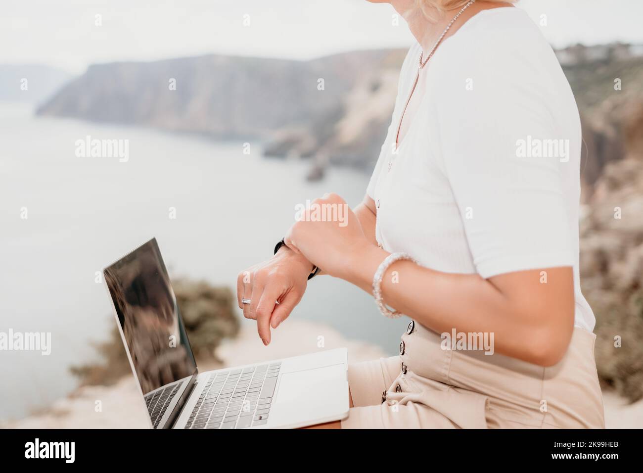 Digital nomad, Business woman working on laptop by the sea. Pretty lady typing on computer by the sea at sunset, makes a business transaction online Stock Photo