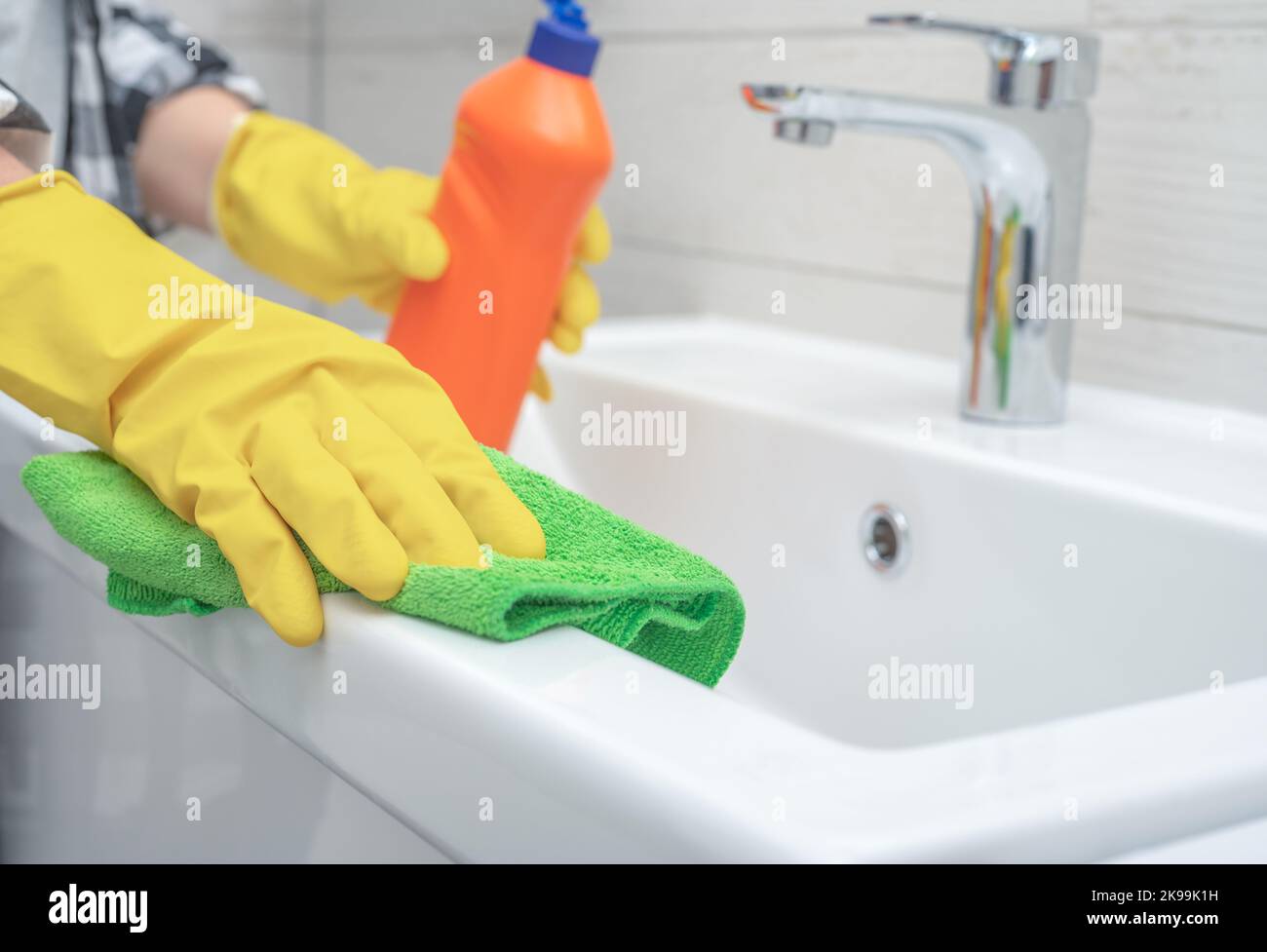 cleaning bathroom sink and faucet with detergent in bathroom. Man doing