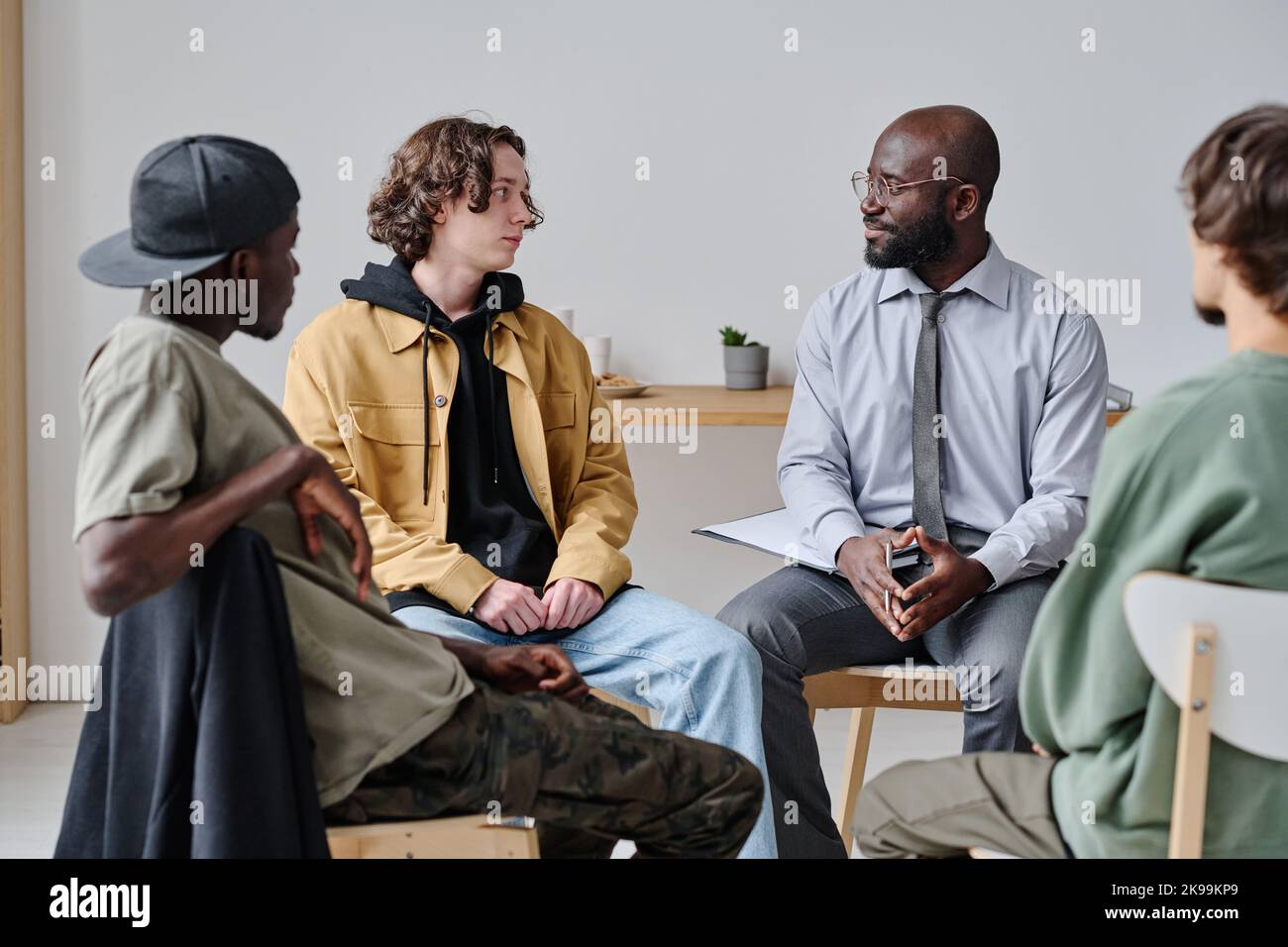 Group of students sitting on chairs and talking to their teacher during psychotherapy at class Stock Photo