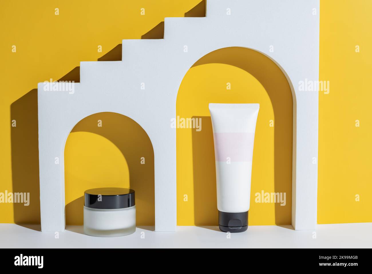 Cosmetic beauty products in white arch on yellow backgeound. Unbranded packaging adv. Cream jar and tube. Stock Photo