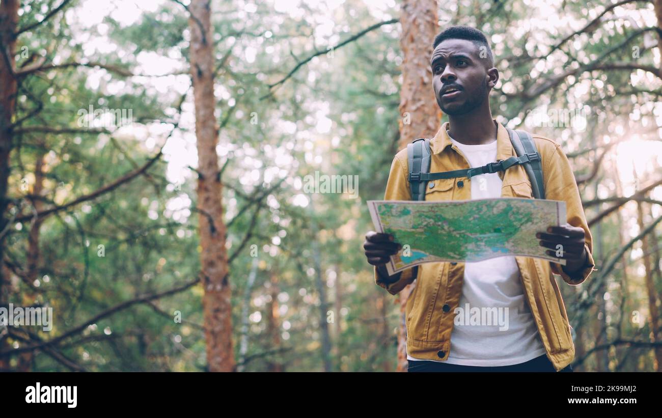 African American man is walking in forest looking at paper map searching for desired tourist destination . Nature, active lifestyle and navigation concept. Stock Photo