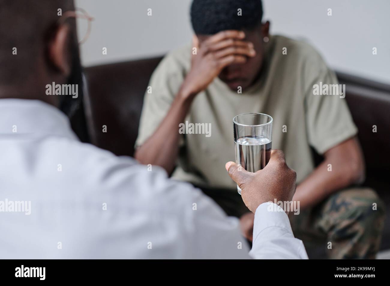 Rear view of psychologist giving glass of water to patient and supporting him during session Stock Photo