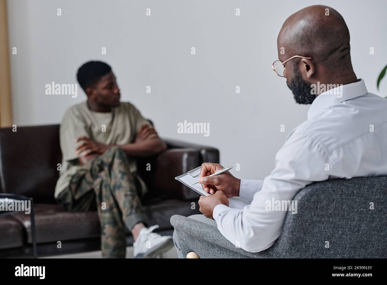 African psychologist making notes sitting on armchair while talking to patient at office Stock Photo