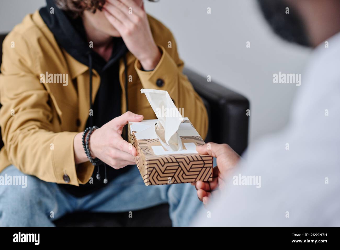 Close-up of young man crying at psychotherapy session while psychotherapist giving tissues Stock Photo