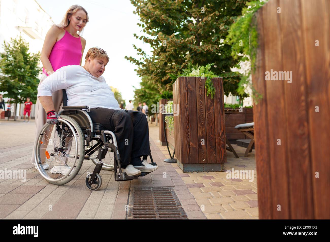 Young female caregiver pushing wheelchair with female person with
