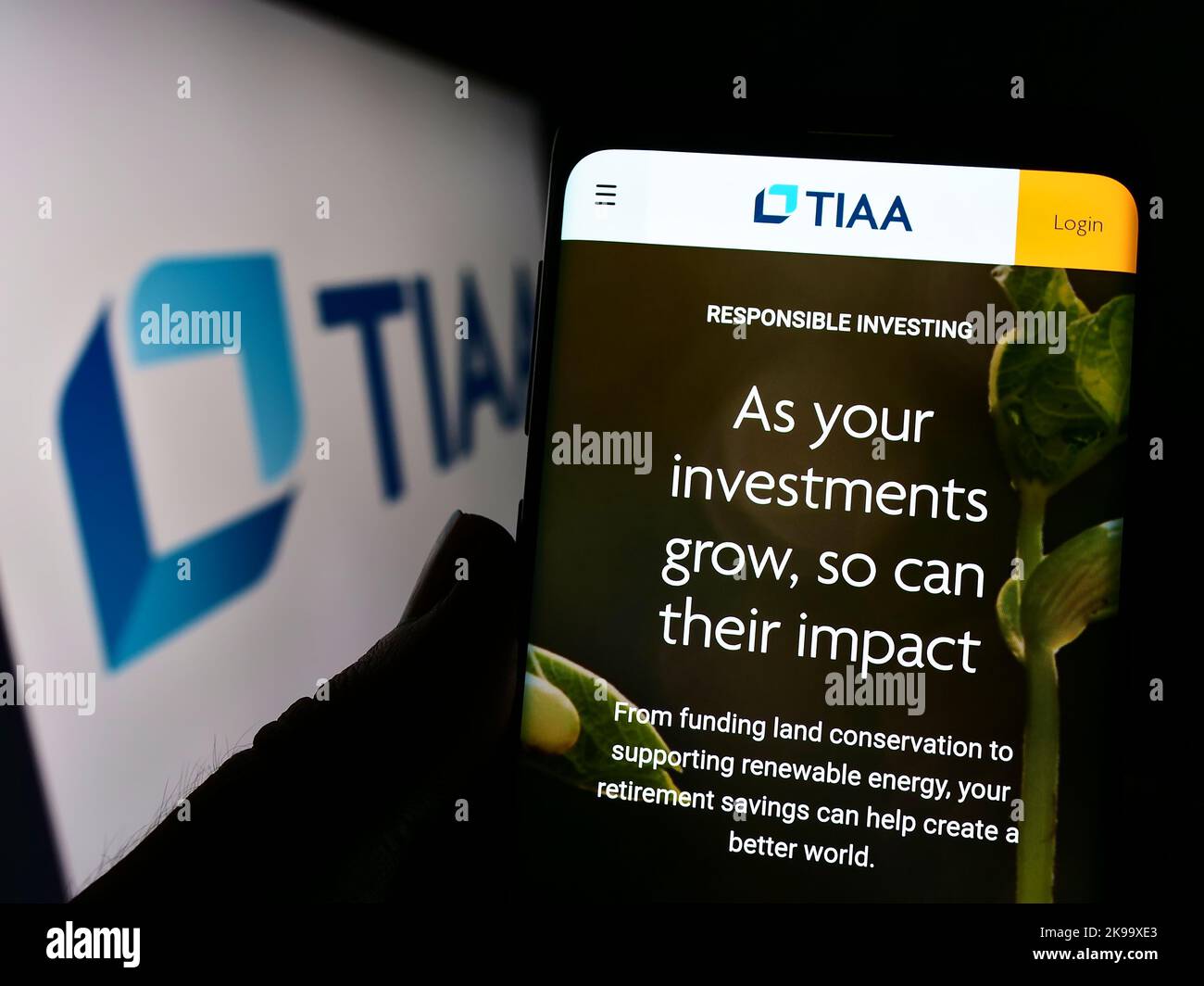 Person holding cellphone with website of US financial services company TIAA on screen in front of logo. Focus on center of phone display. Stock Photo