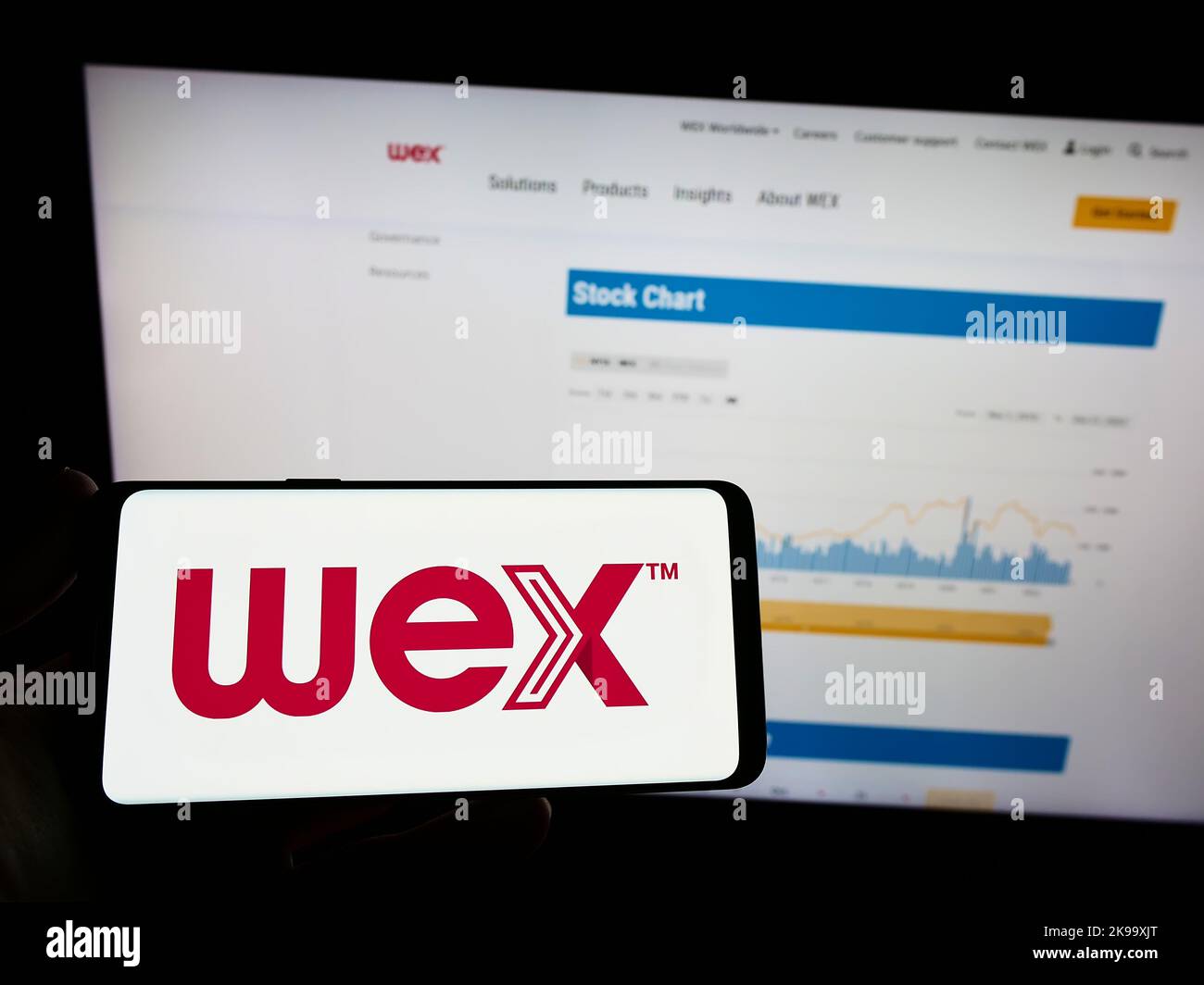 Person holding mobile phone with logo of American payment processing company WEX Inc. on screen in front of web page. Focus on phone display. Stock Photo