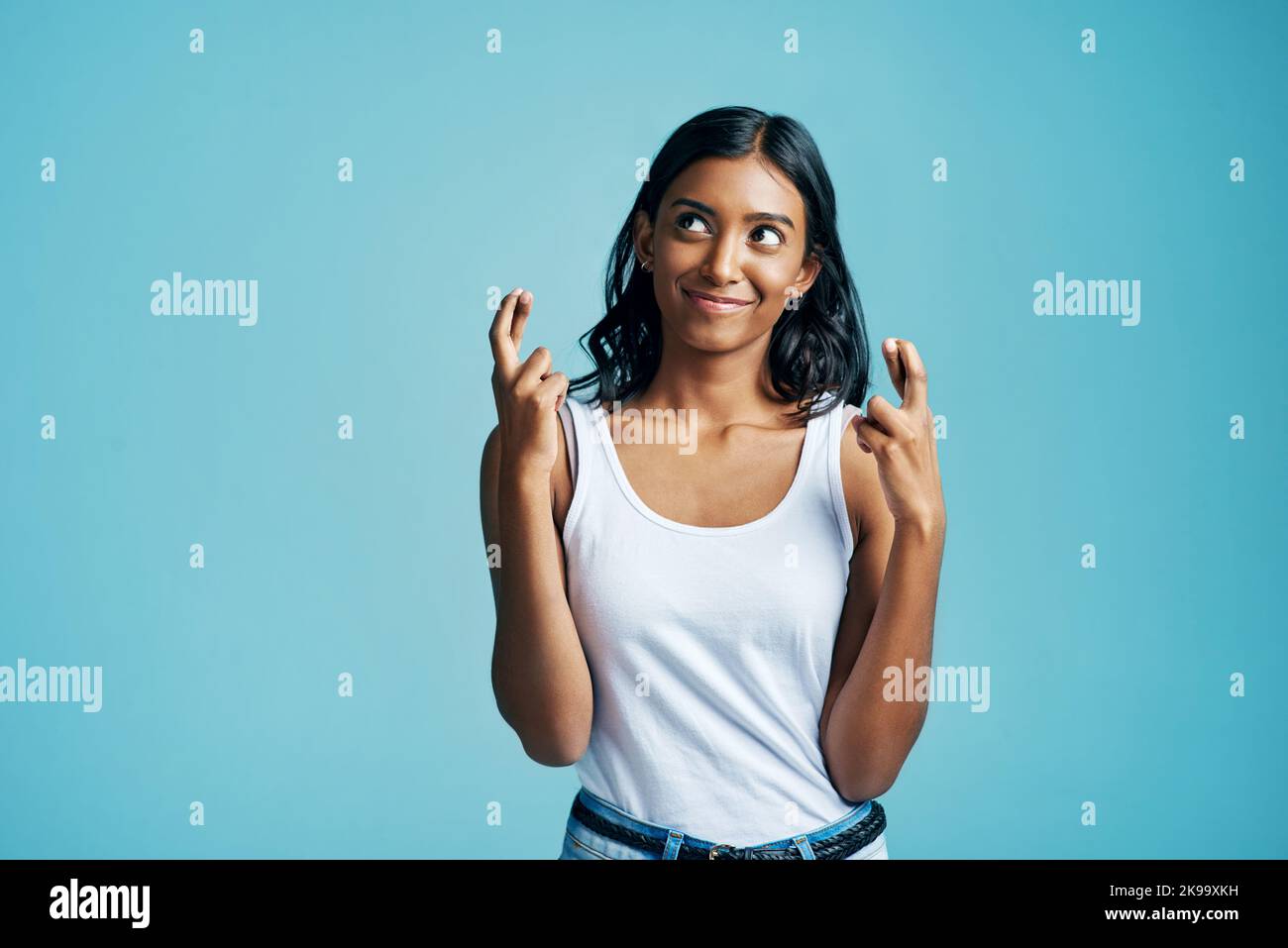 Hoping beyond all hope. Studio shot of a beautiful young woman crossing her fingers against a blue background. Stock Photo