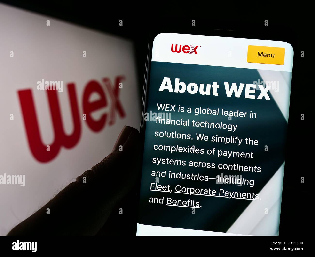 Person holding cellphone with webpage of US payment processing company WEX Inc. on screen in front of logo. Focus on center of phone display. Stock Photo