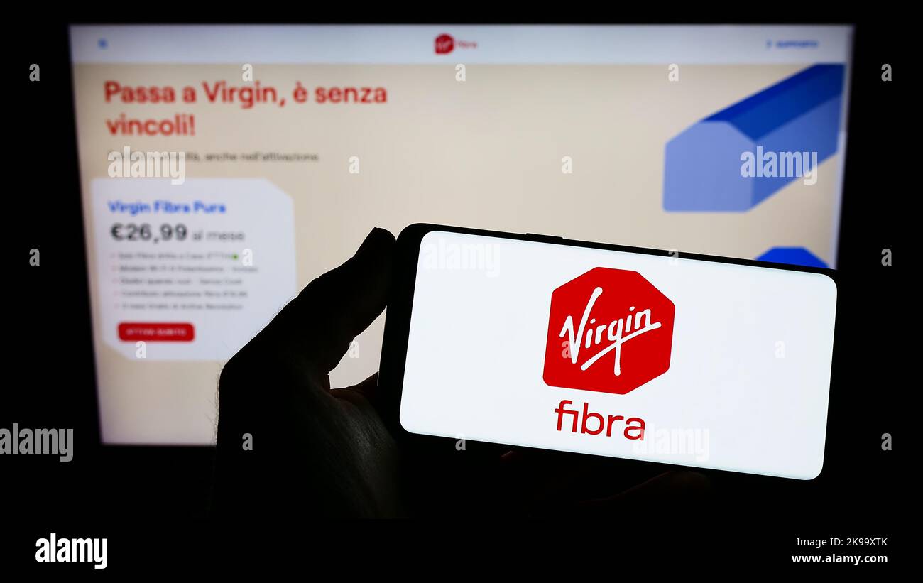 Person holding smartphone with logo of Italian company Virgin Fibra S.r.l. on screen in front of website. Focus on phone display. Stock Photo