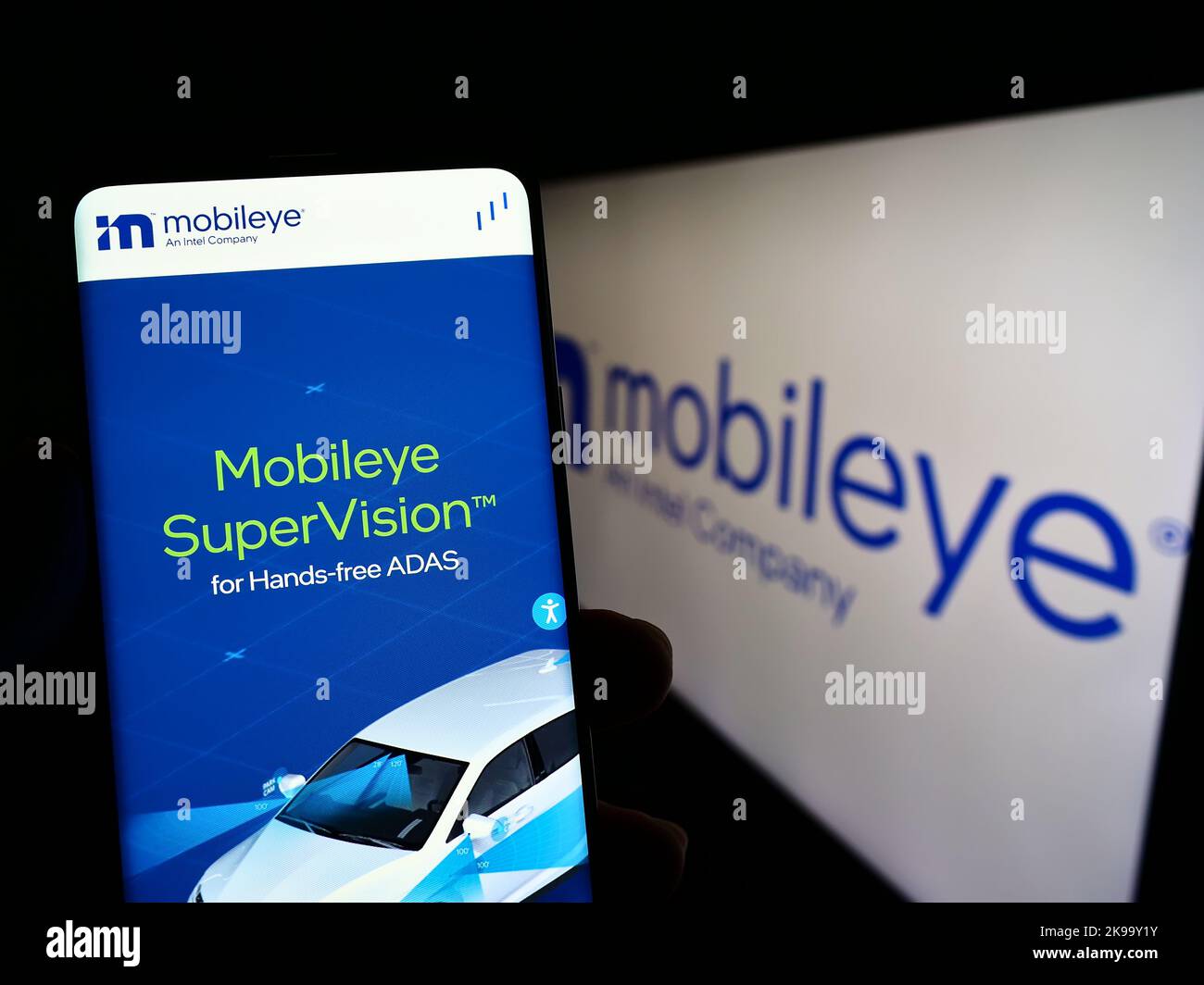 Person holding cellphone with website of Israeli autonomous driving company Mobileye on screen in front of logo. Focus on center of phone display. Stock Photo