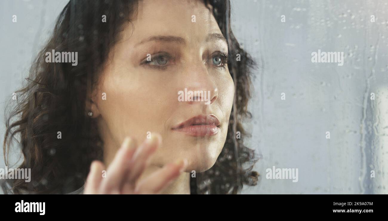 Its never easy dealing with a bad breakup. a sad young woman standing by a window while its raining outside. Stock Photo
