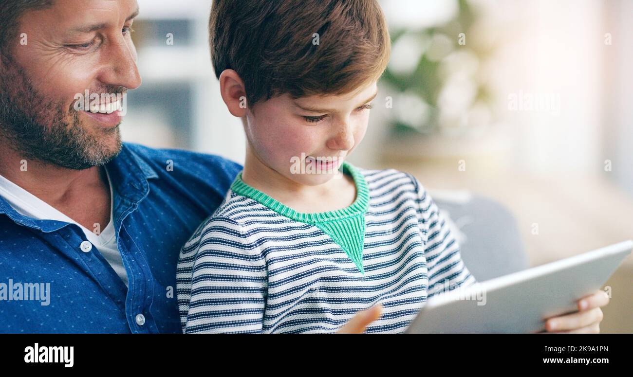 Hes teaching me about the app world. an adorable little boy sitting on his fathers lap and using a digital tablet at home. Stock Photo