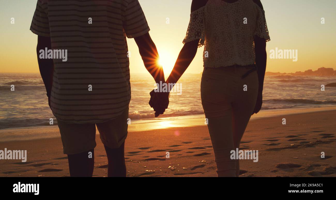We complete each others lives. Rearview shot of an unrecognizable young couple holding hands on the beach at sunset. Stock Photo