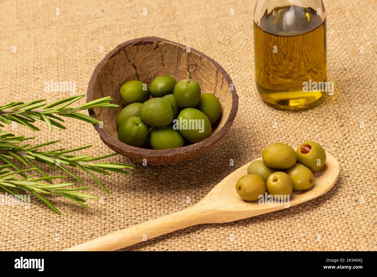 Green olives in wooden spoon and in coconut shell. Olive oil in bottle ...