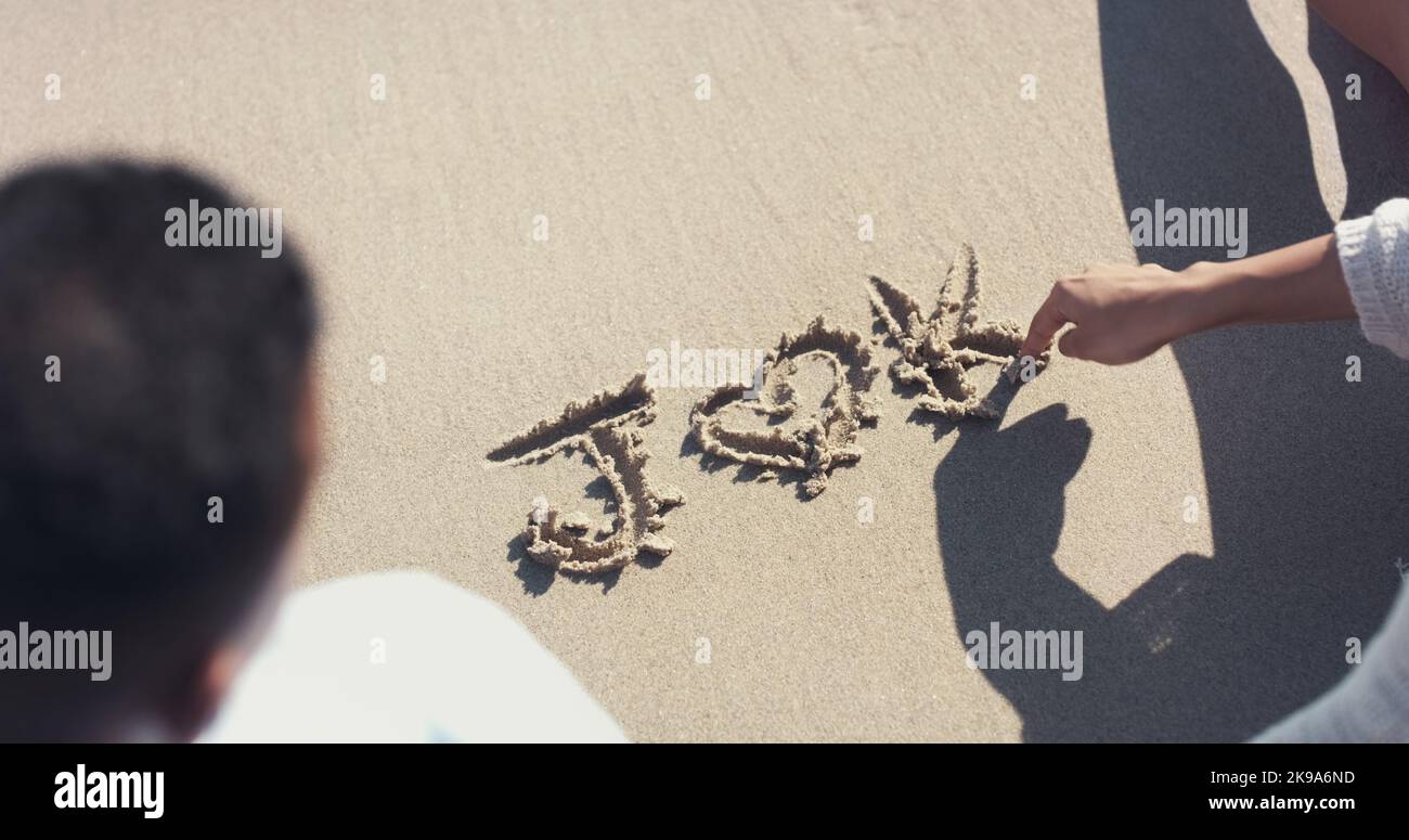 Theyll love each other forever. High angle shot of an unrecognizable couple writing out their initials on sand at the beach. Stock Photo