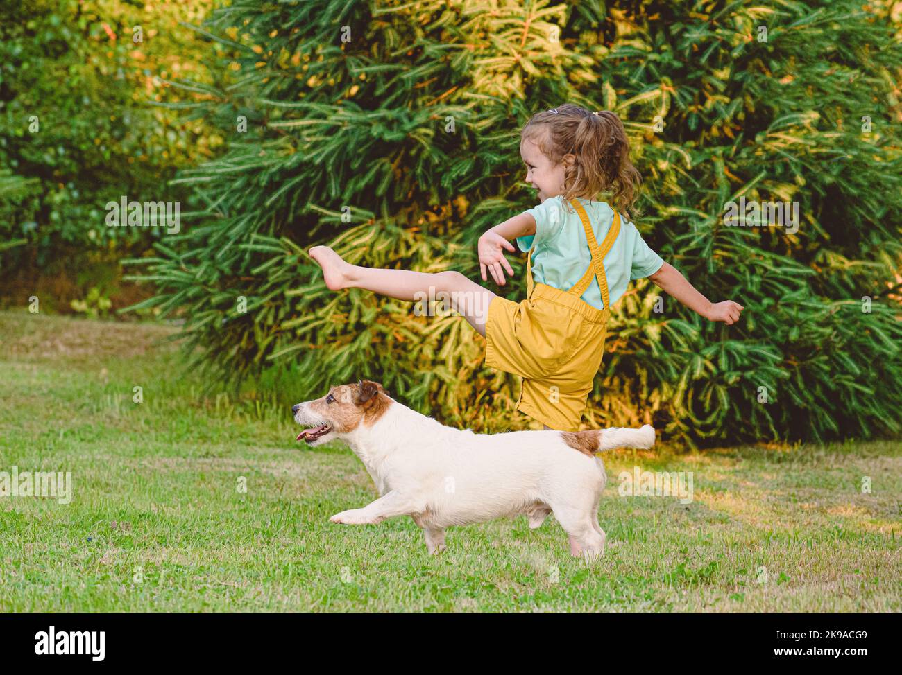 Little girl workouts together with her pet dog at backyard lawn Stock Photo