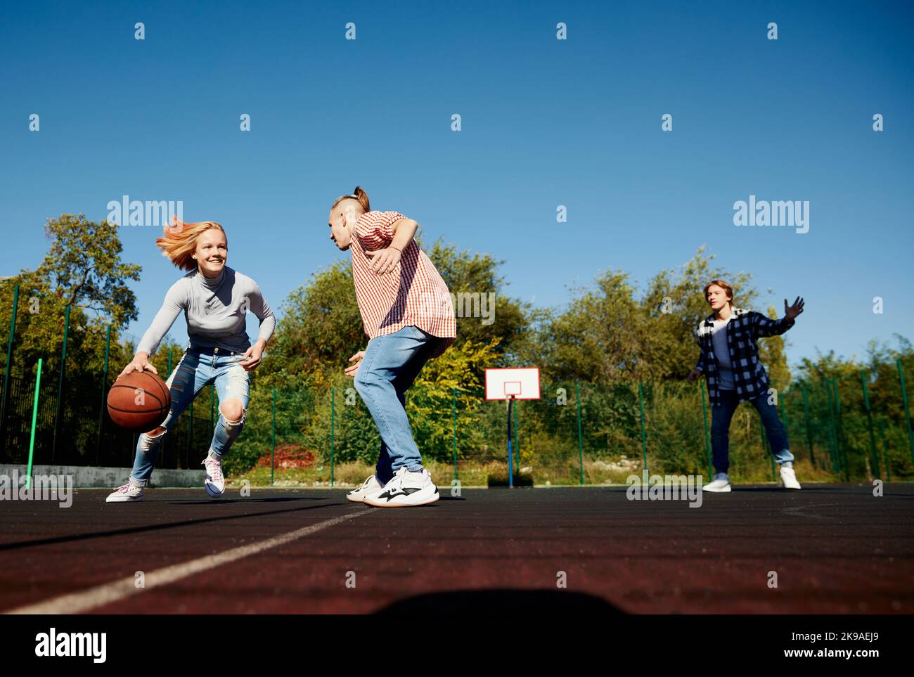 Three teenagers playing streetball with basketball ball at school yard after classes. Concept of sport, leisure activities, hobbies, team, friendship Stock Photo