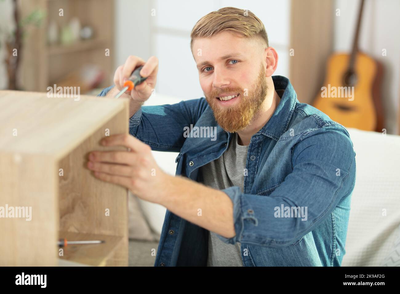 man assembling furniture at home using a screwdriver Stock Photo