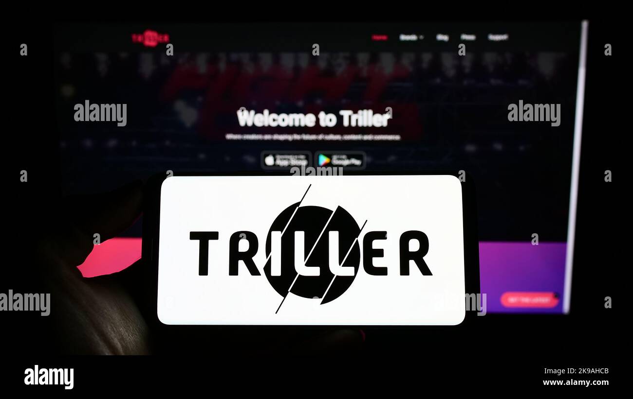 Person holding cellphone with logo of US video sharing company Triller Inc. on screen in front of business webpage. Focus on phone display. Stock Photo