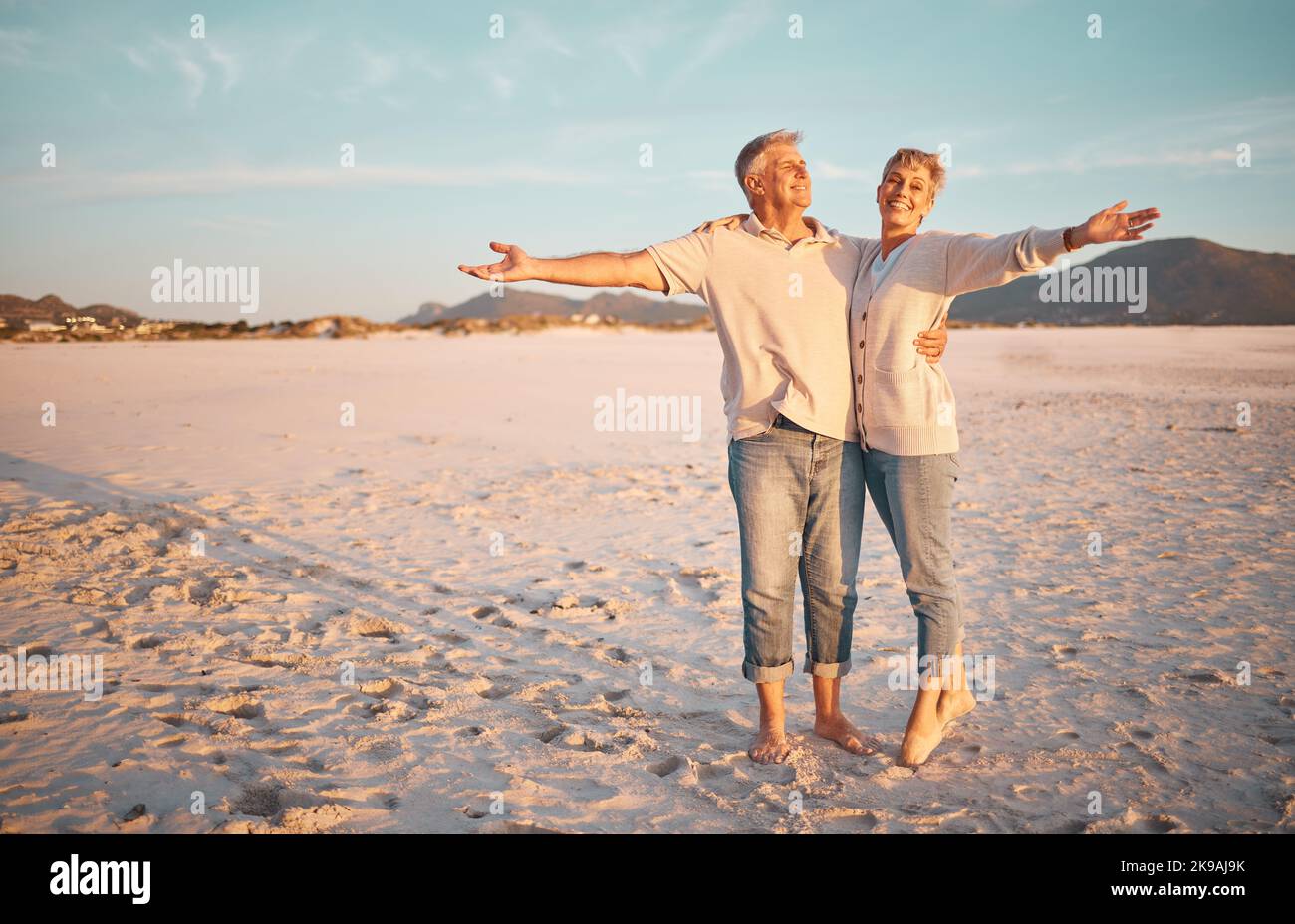Love, beach and summer with a senior couple standing together on the sand on a sunny day. Travel, vacation and romance with a n elderly man and woman Stock Photo