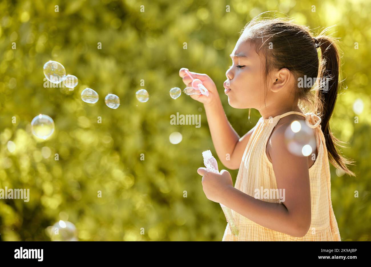 Bubbles, outdoor and girl in a nature park feeling relax, playful and content by sunshine. Child from Taiwan blow a bubble in the spring sun feeling Stock Photo