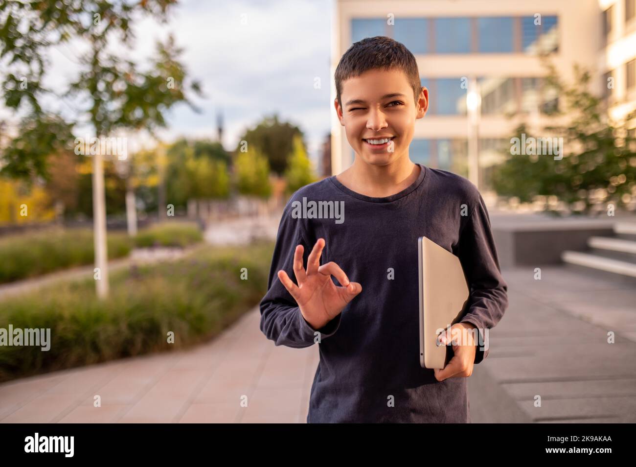 Teen showing a hand gesture and smiling at somebody outdoors Stock Photo
