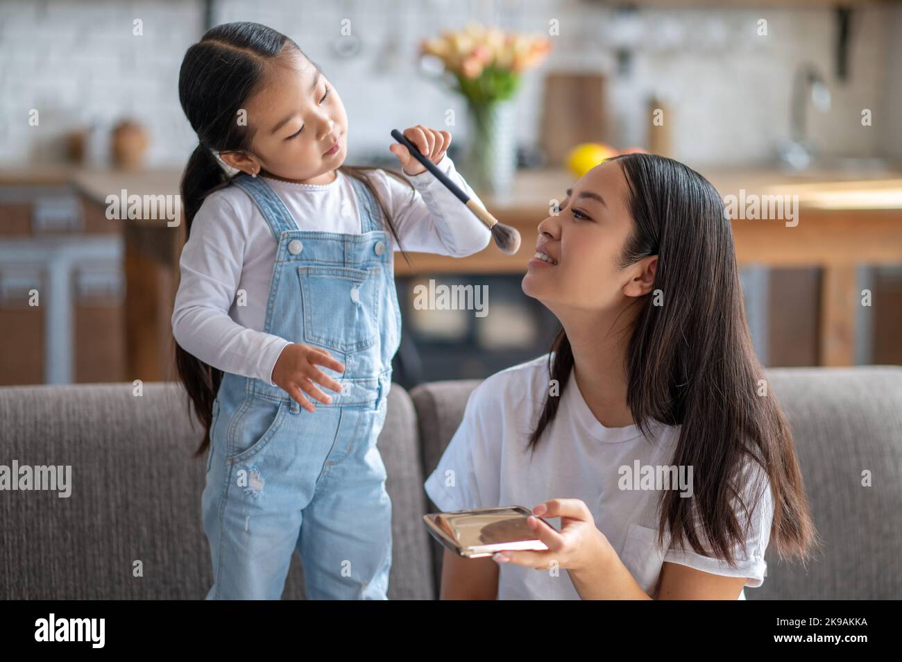 Caring child applying the compact powder to her female parent Stock
