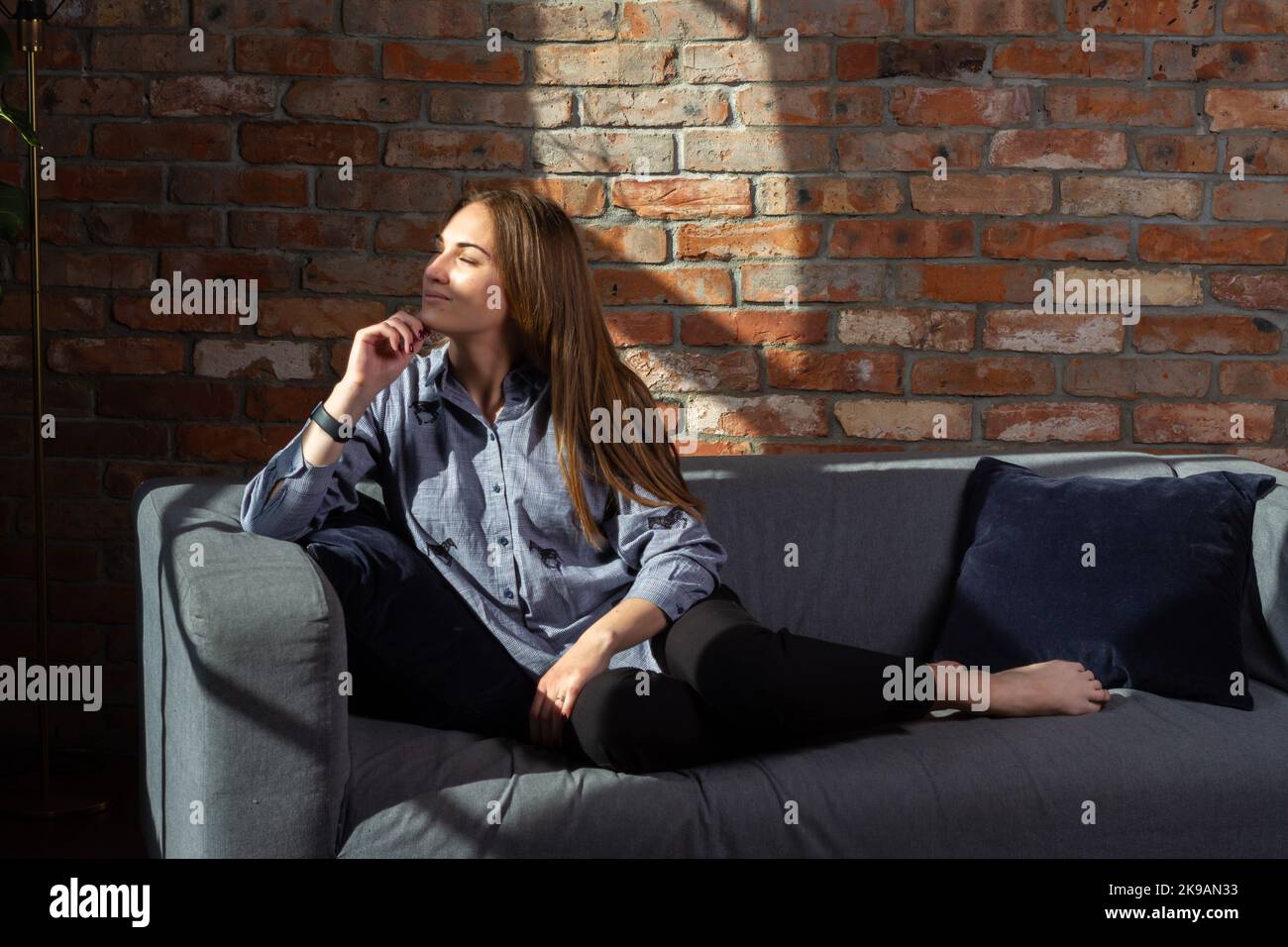 Woman in a blue shirt on the couch dreaming in the sunlight coming from windows Stock Photo