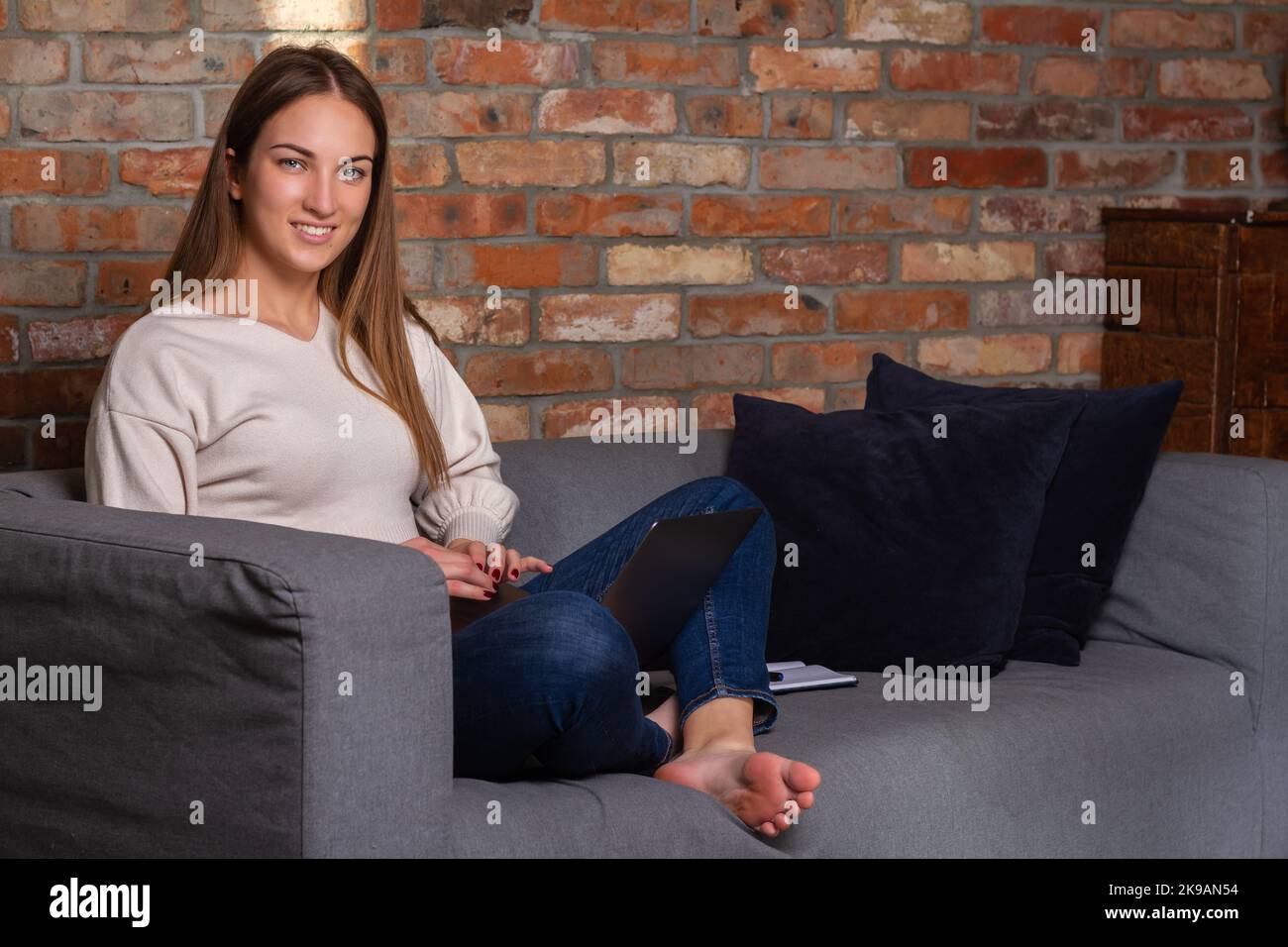 Smiling woman in a white sweater with a laptop and a notebook on her side Stock Photo