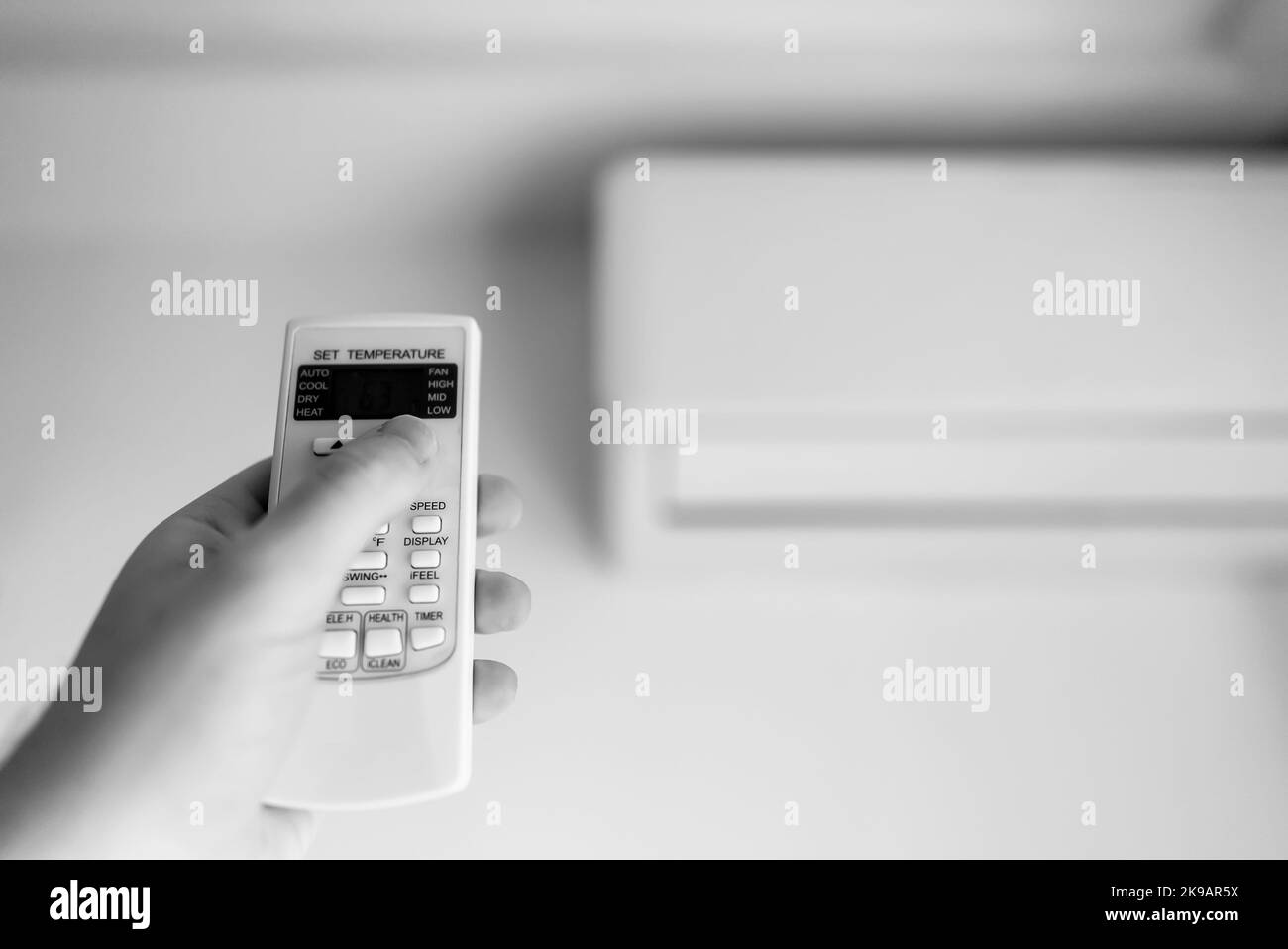 Hand holding remote control aimed at the air conditioner. Stock Photo