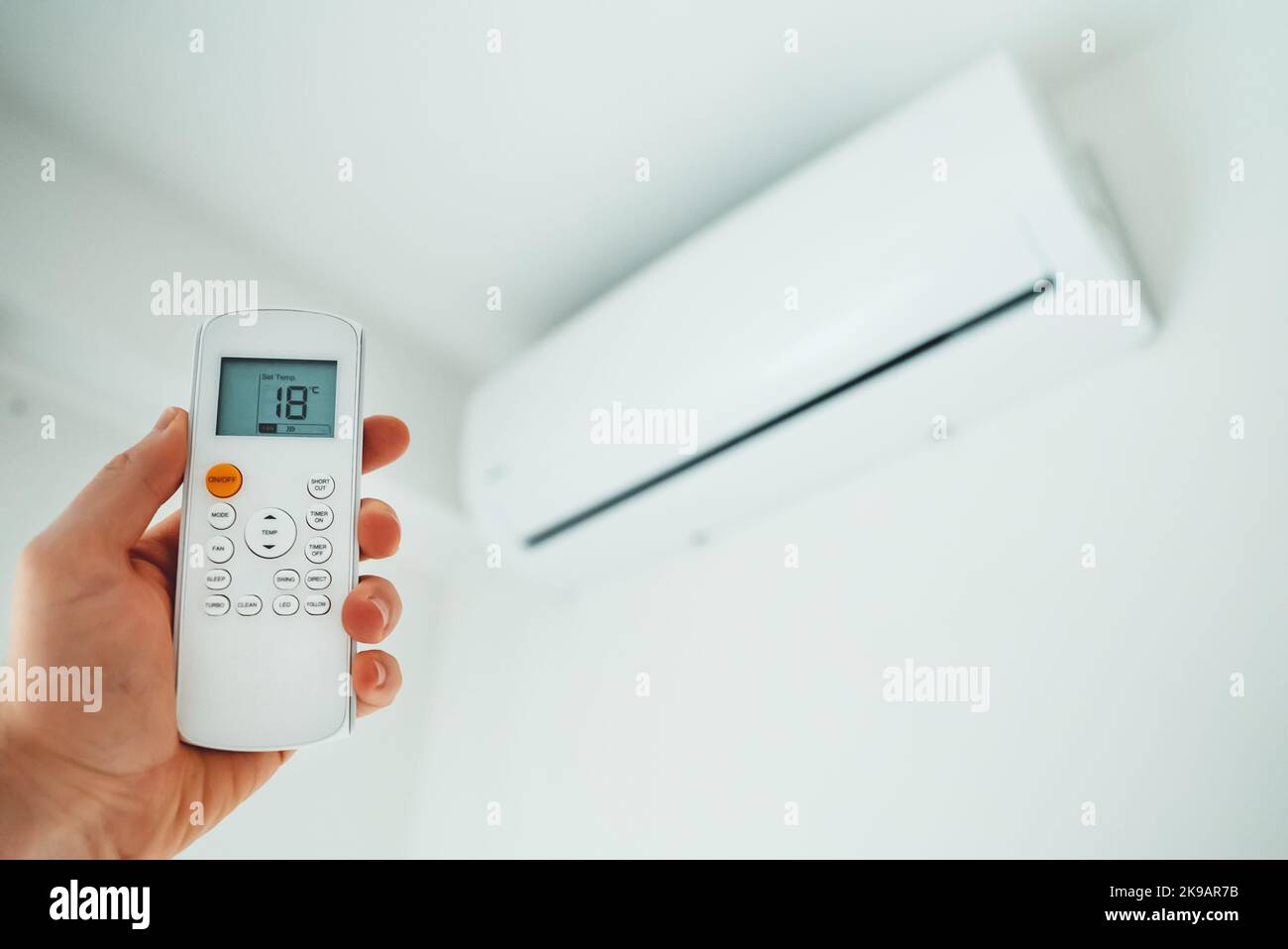 Hand holding remote control aimed at the air conditioner. Stock Photo