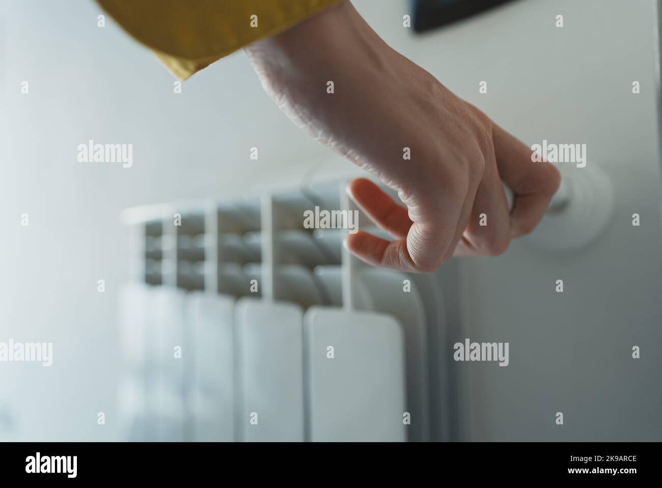 Female hand adjusting thermostat to turn on the radiator heater at home. Stock Photo