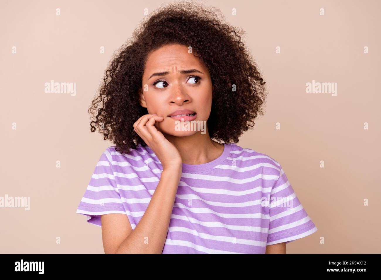 Photo of thoughtful doubtful girl dressed purple t-shirt looking empty space biting lip isolated beige color background Stock Photo