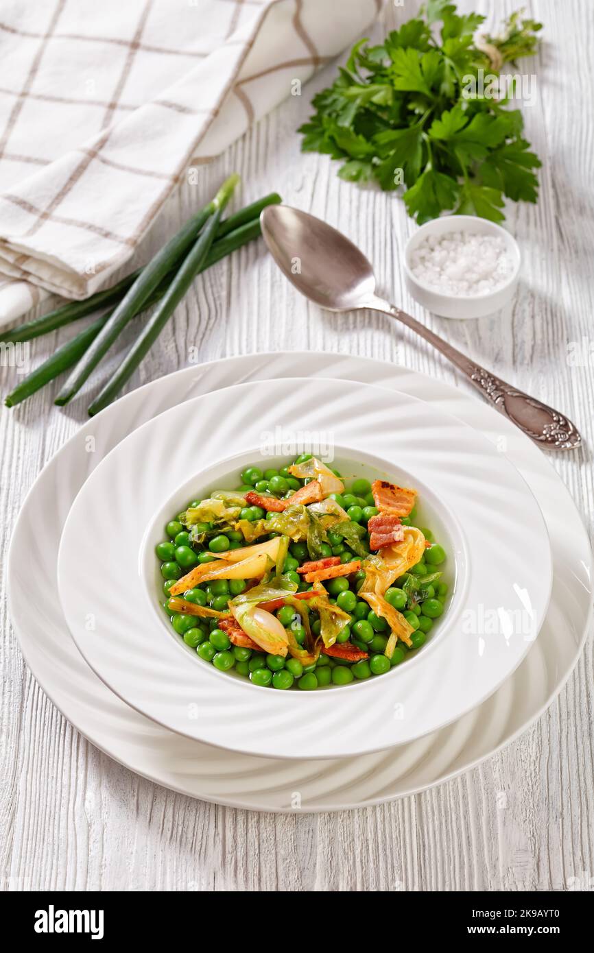 petits pois, french dish of tender, new-season peas braised in chicken stock with lettuce, onion bulbs and speck, cut into lardons, served in white bo Stock Photo