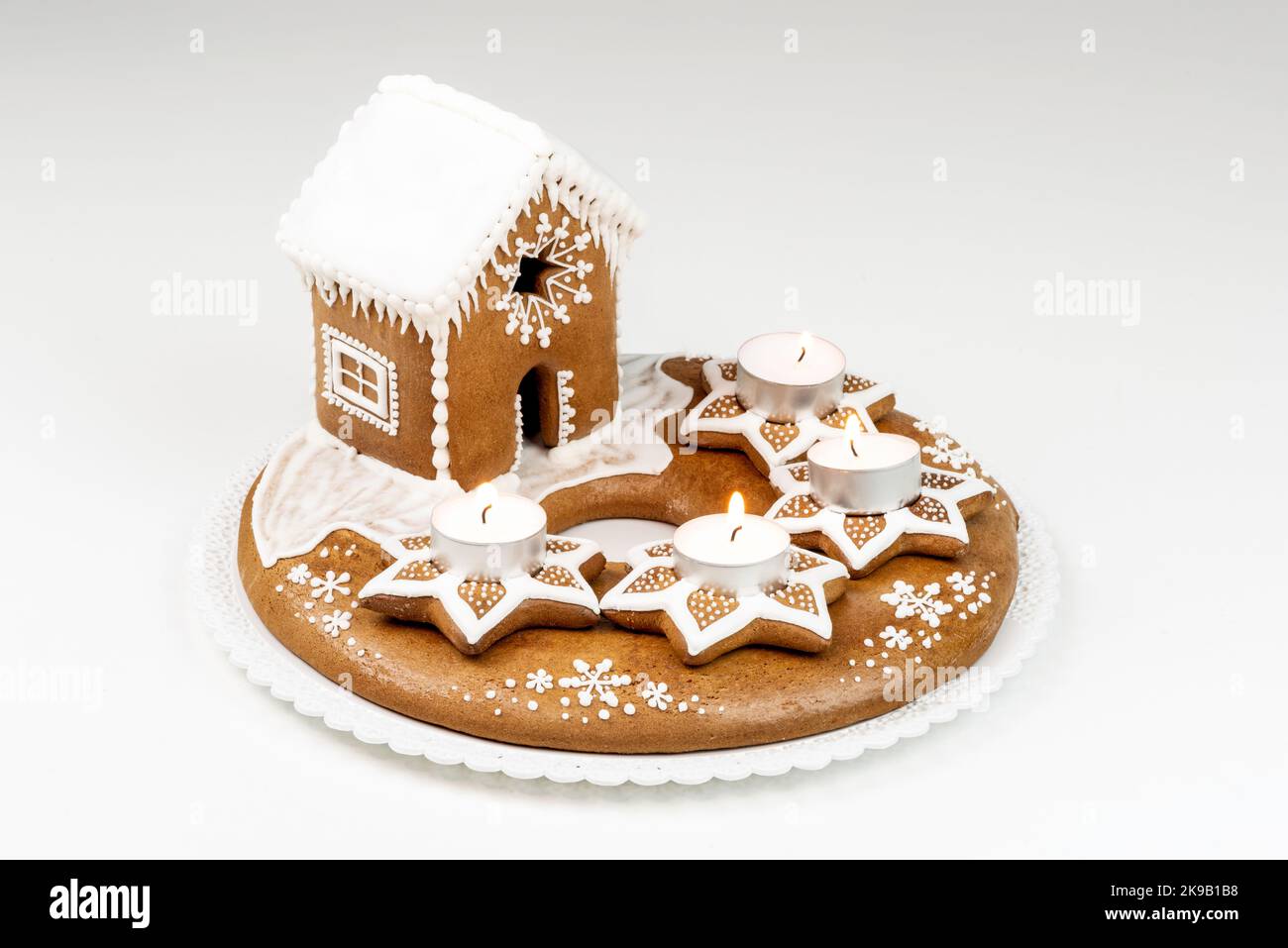 Isolated advent candlestick with four lighted candles and christmas homemade gingerbread house on white background Stock Photo