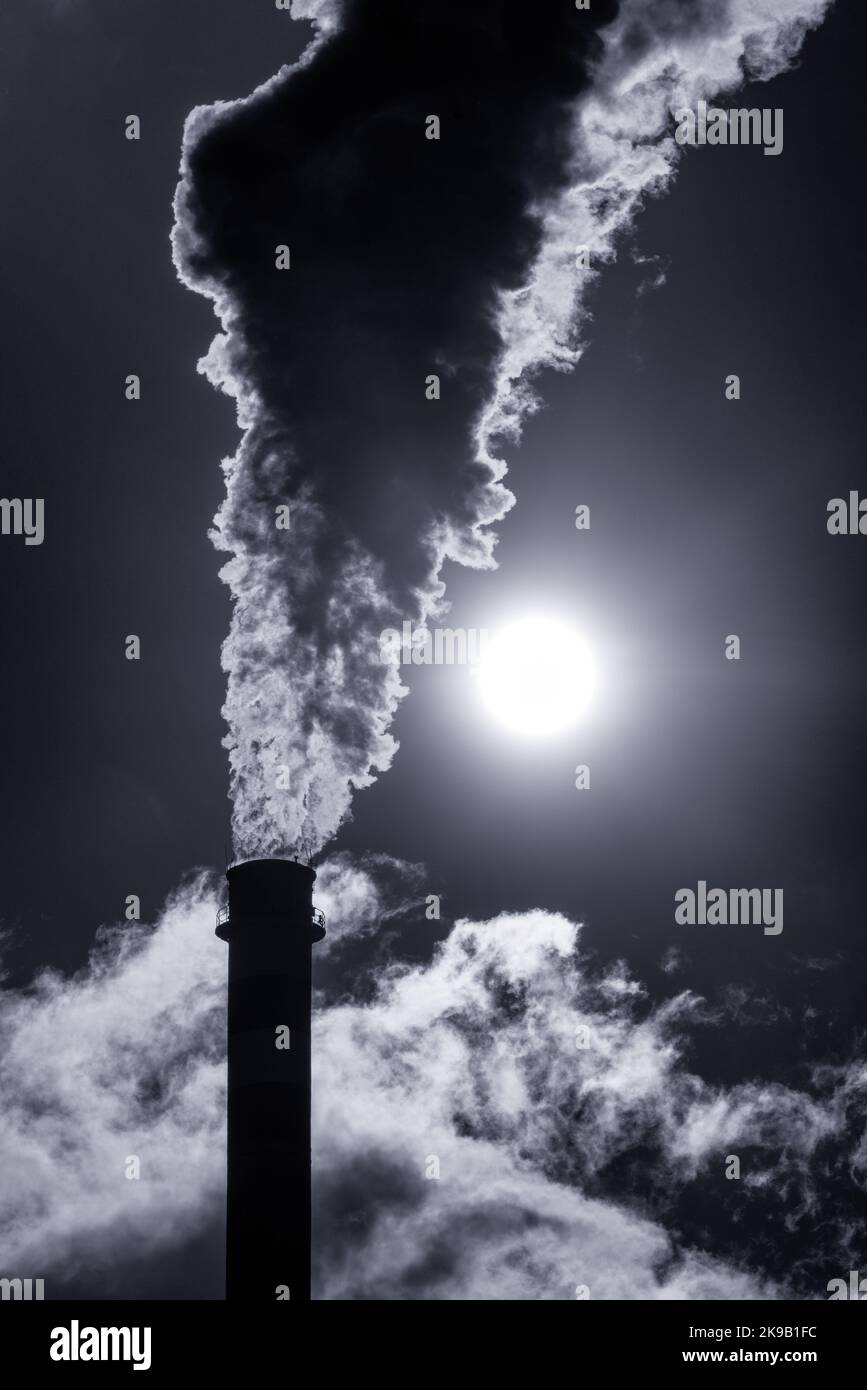 Dark smoke and steam from chimney in factory against the sun on sky Stock Photo