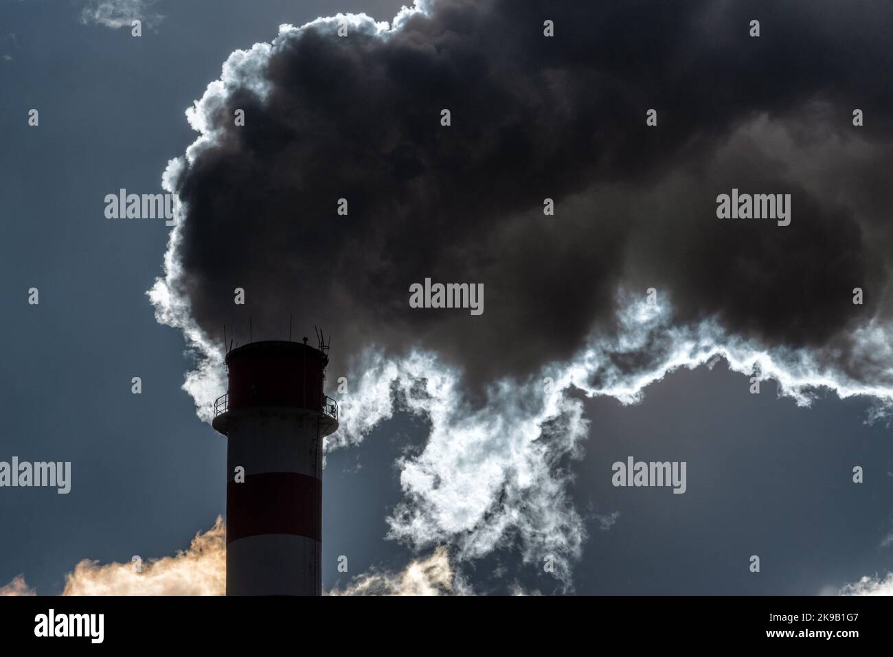 Dark smoke and steam from chimney in factory against the sky Stock Photo