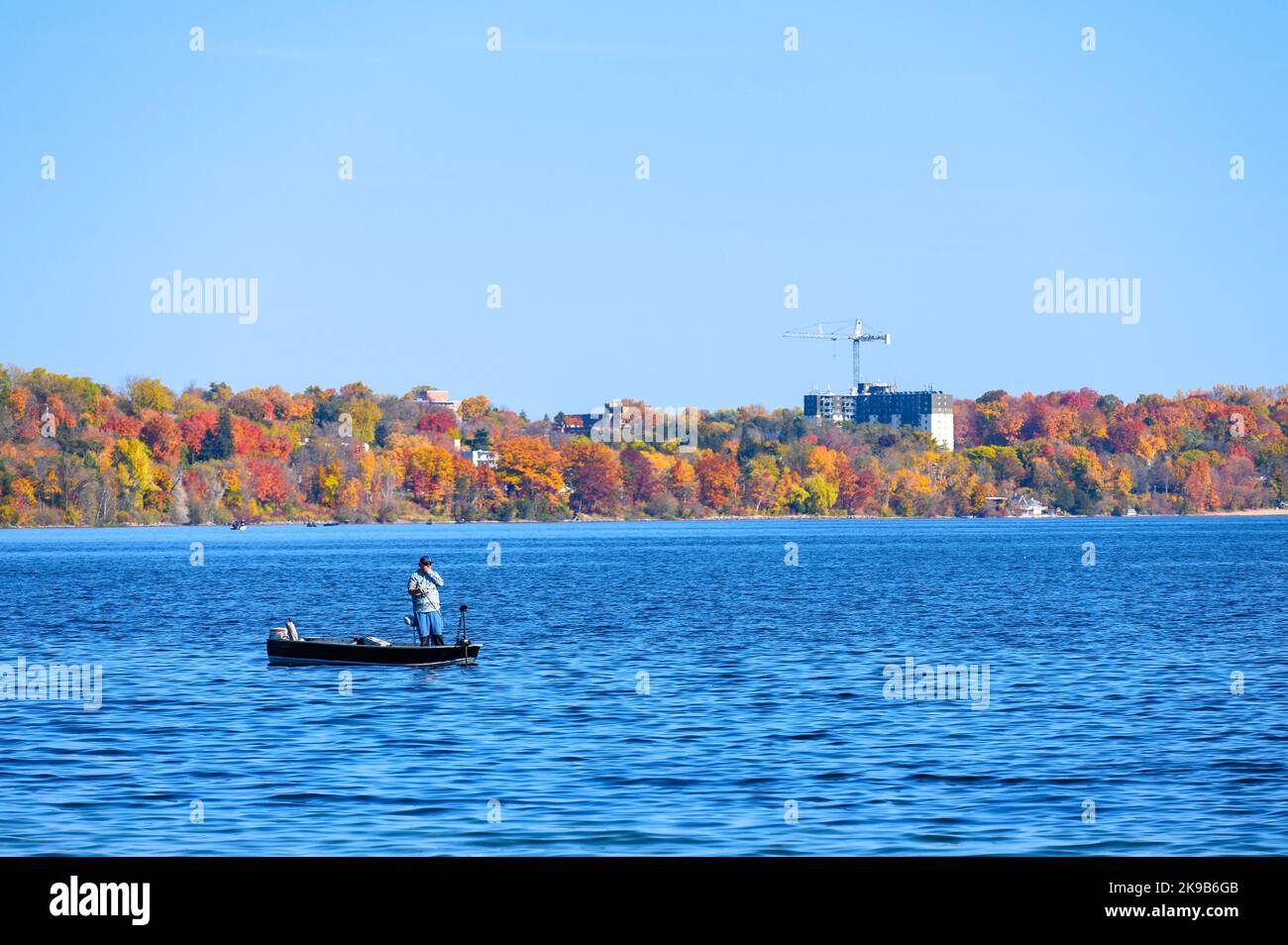 A man using a small boat to fish in Lake Simcoe. The autumn colors are seen in the background Stock Photo
