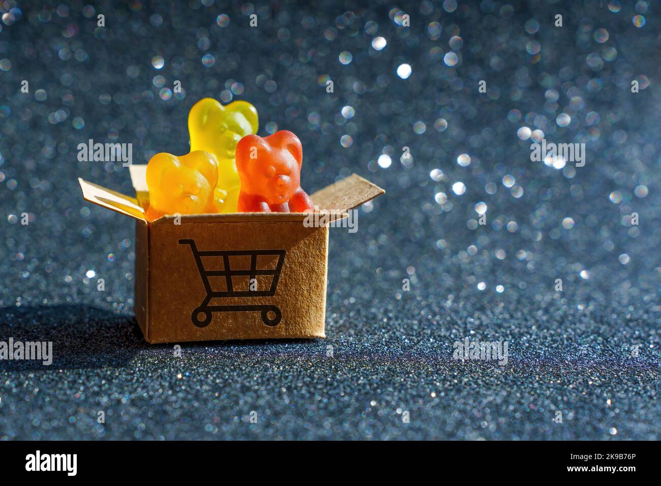 Three colorful gummy bear candies in a tiny shipping box labeled with a shopping cart symbol. Stock Photo