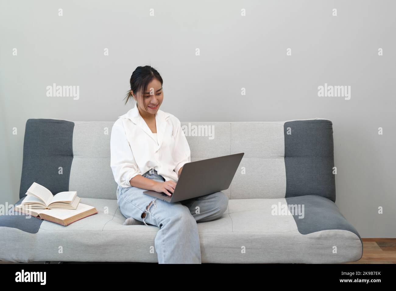 Portrait of a young Asian woman sitting on the sofa using a computer ...